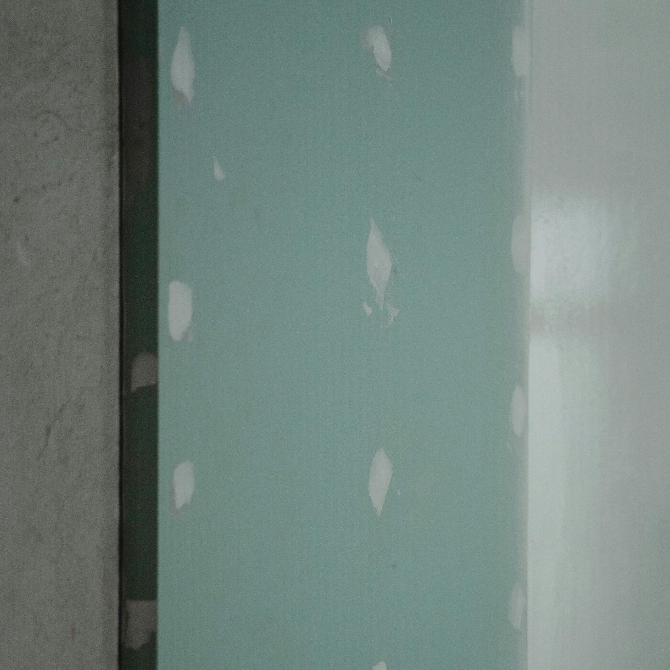 pexels photo 6474207 6474207 Freshly installed green drywall with white patches, ready for painting or finishing touches in home renovation.
